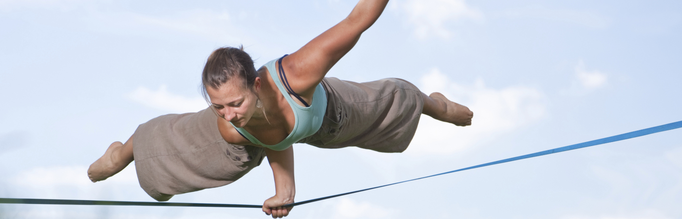A person balancing with one warm on a taut wire several feet above the ground